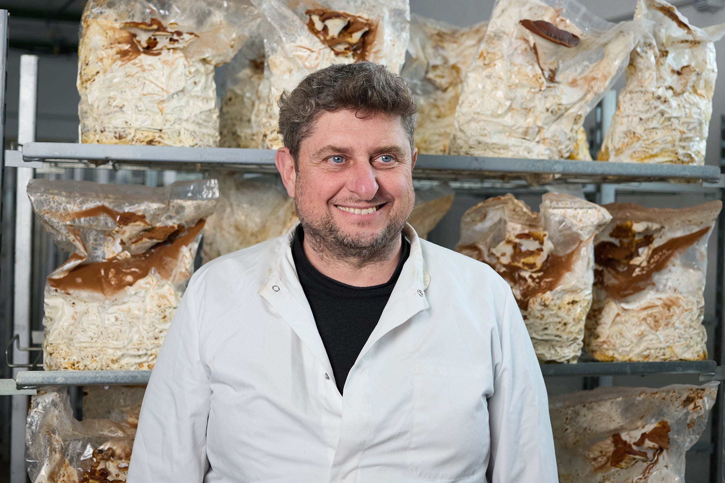 Produttore Virtus Mushroom in camice bianco davanti alle scaffalature di coltivazione dei funghi